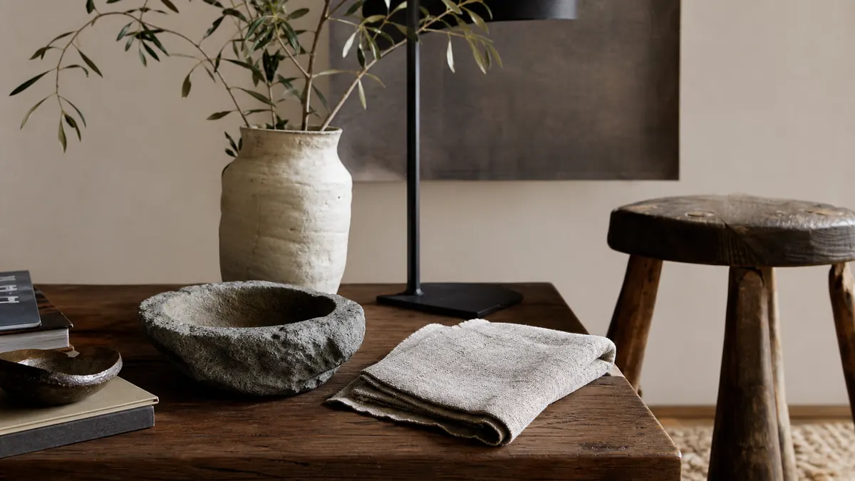An organic modern living room with warm wood, linen upholstery, stone texture, a sculptural lamp, handmade ceramics, and relaxed natural light